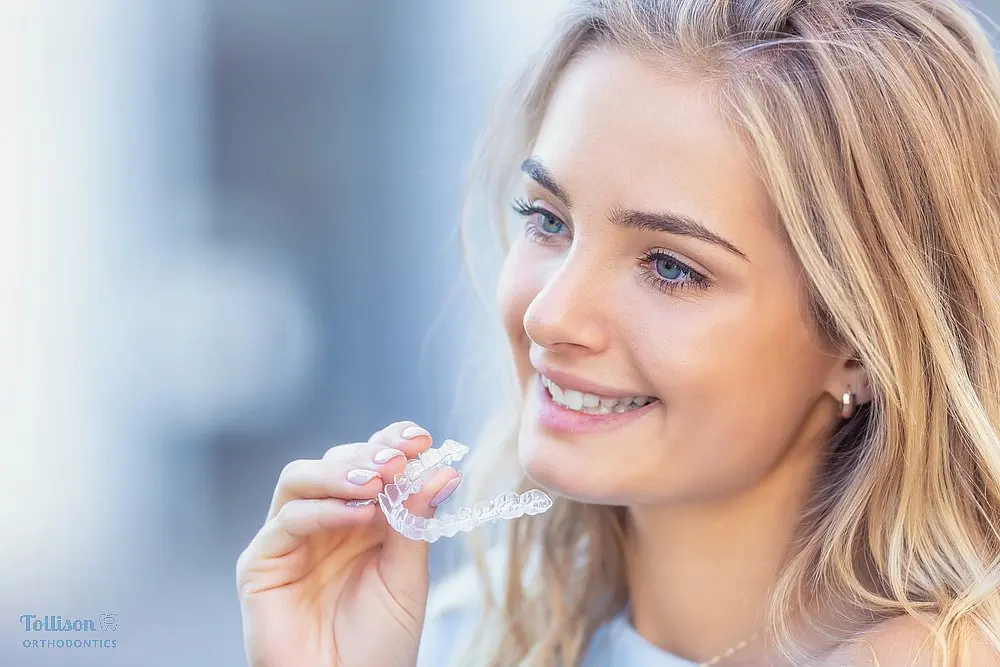 Close-up of smiling woman holding a clear Invisalign tray, highlighting orthodontic care with invisible aligners illustrating Does Insurance Cover Invisalign in Greenville, SC