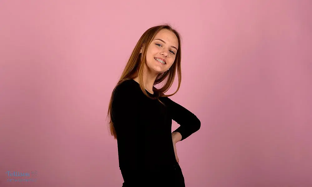 Confident young woman posing against a pink background, smiling naturally after her braces for overbite in Greenville, SC treatment.