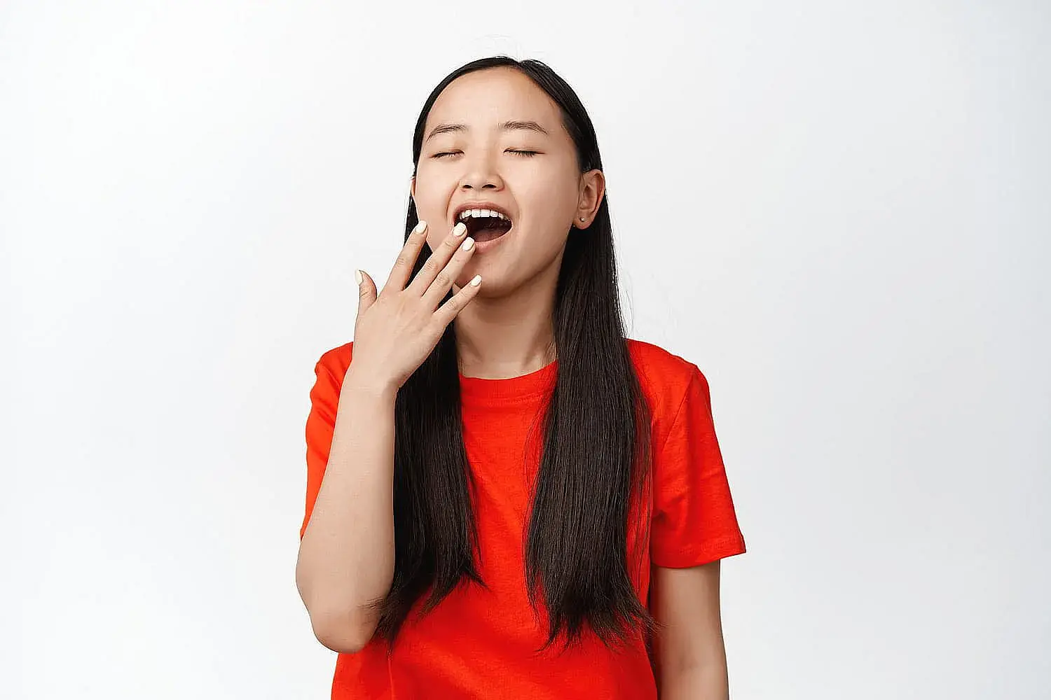 A person in a red shirt yawns with eyes closed, covering their mouth with one hand against a plain background, slightly revealing an underbite, indicating mouth breathing in Greenville, SC A person in a red shirt yawns with eyes closed, covering their mouth with one hand against a plain background, slightly revealing an underbite, indicating mouth breathing in Greenville, SC