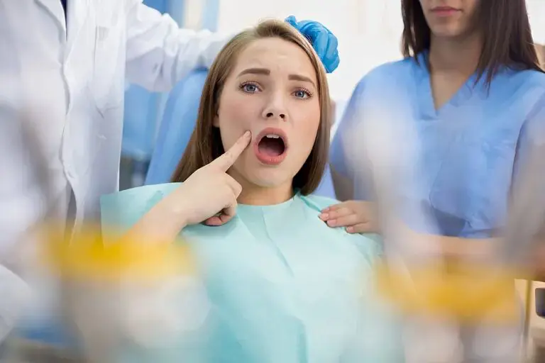 A teenager with curly hair, braces, and a light peach shirt over a white t-shirt stands smiling and waving in front of a blue background at Tollison Orthodontics in Greenville, SC. Wondering how long do braces take in Greenville?.