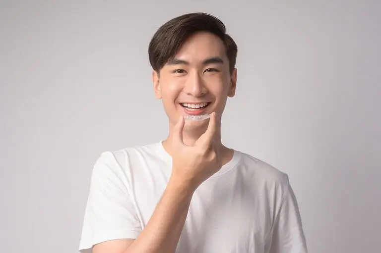 young smiling man holding invisalign clear aligners braces white background studio dental - How Does Invisalign Work in Greenville, SC