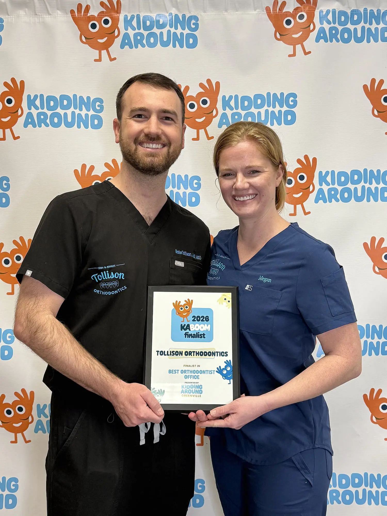 Dr. Blake Tollison and another person in scrubs hold a 2024 KABOOM "Best Orthodontist" award for Tollison Orthodontics in Greenville, SC.