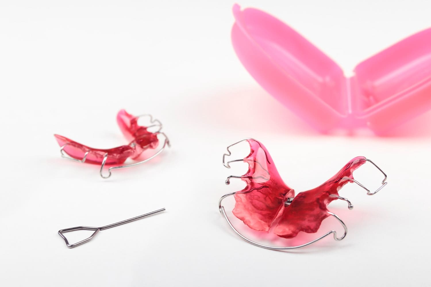 Two red dental retainers rest on a white surface beside a pink, open retainer case, reminiscent of a visit to the children's orthodontist. A small wire tool is also visible nearby in Greenville, SC