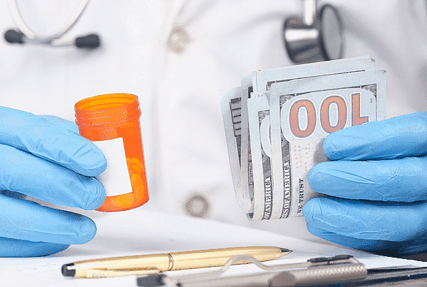 A person wearing blue gloves holds a pill bottle in one hand and a stack of hundred-dollar bills in the other, hinting at a financial decision. A stethoscope and pen lie nearby, perhaps indicating options like an Invisalign payment plan in this medical context in Greenville, SC