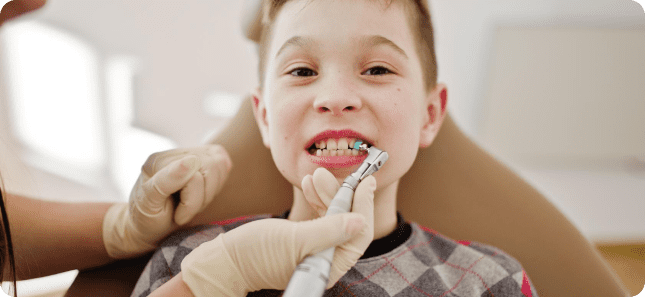 A child sits in a dental chair while an orthodontist carefully uses a dental tool in their mouth. The child is wearing a patterned shirt, and the dentist, clad in gloves, works with precision in Greenville, SC