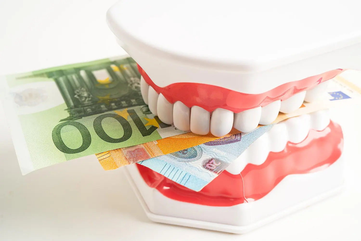 Toy chattering teeth, as if promoting orthodontic insurance plans, grip euro banknotes tightly in their mouth in Greenville, SC