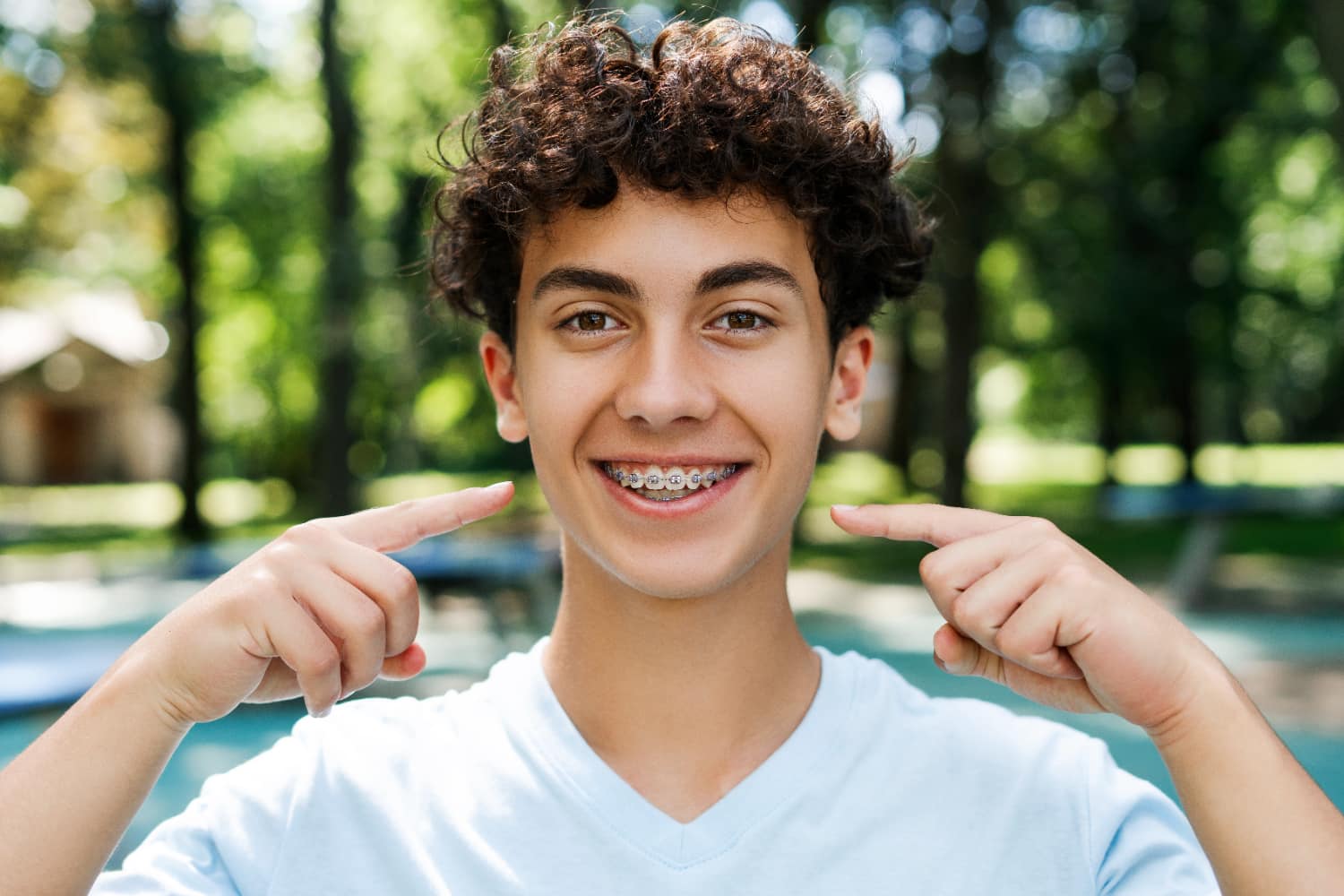 Teen smiling outdoors, proudly pointing to the braces on their teeth courtesy of Tollison Orthodontics in Greenville, SC