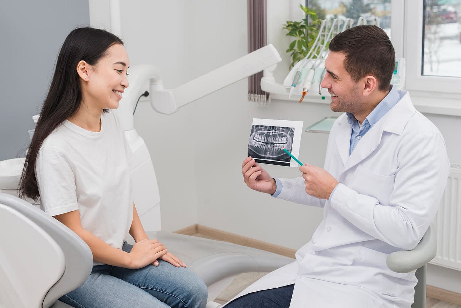 The dentist is discussing a dental X-ray with the patient, highlighting areas of interest in the examination room, potentially considering jaw surgery for optimal oral health in Greenville, SC
