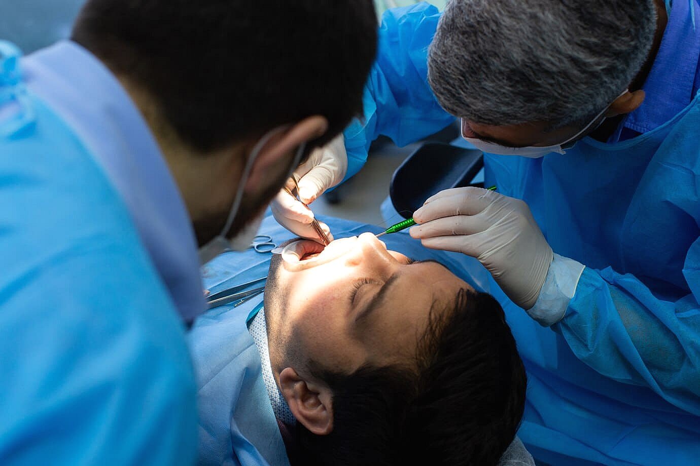 Two dental professionals in blue gowns and masks perform a procedure on a patient lying in a dental chair, carefully addressing issues related to tongue thrust in Greenville, SC