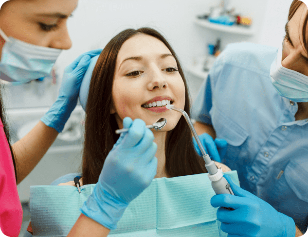 A woman is receiving dental treatment focused on adult orthodontics from two attentive dentists, both wearing masks and gloves, in a modern clinic in Greenville, SC