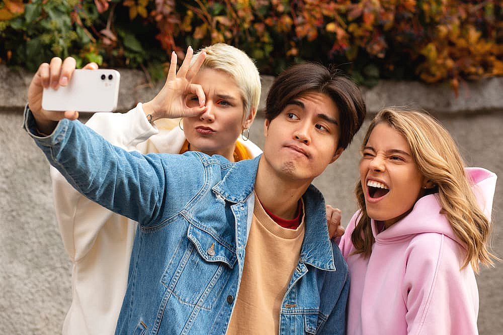 Three friends taking a selfie outside, one making a hand gesture, another looking amused while discussing different types of braces, and the third smiling widely in Greenville, SC