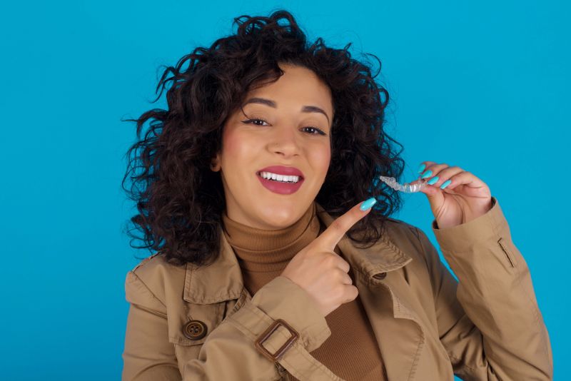 A woman smiling proudly presents a clear dental aligner hold with her hand, reminiscent of modern invisalign at Tollison Orthodontics in Greenville, SC