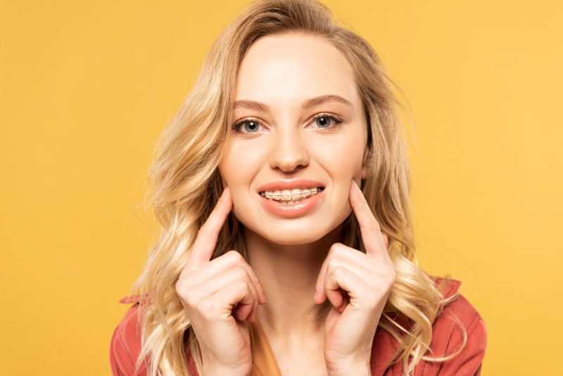 A woman pointing to her braces after receiving expert care clear brace from a dentist at Tollison Orthodontics in Greenville, SC