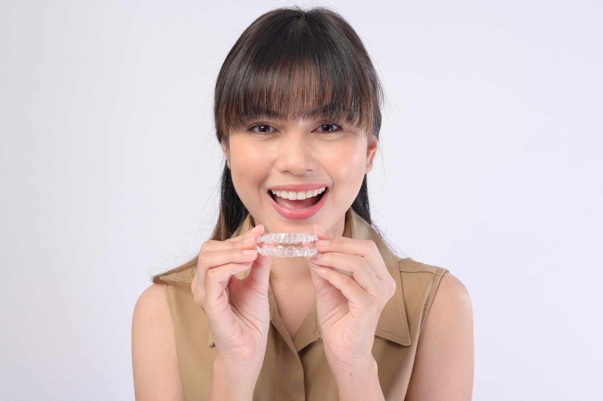 A person smiling and holding an Invisalign clear dental aligner near their mouth, showcasing the benefits of adult orthodontics in Greenville, SC