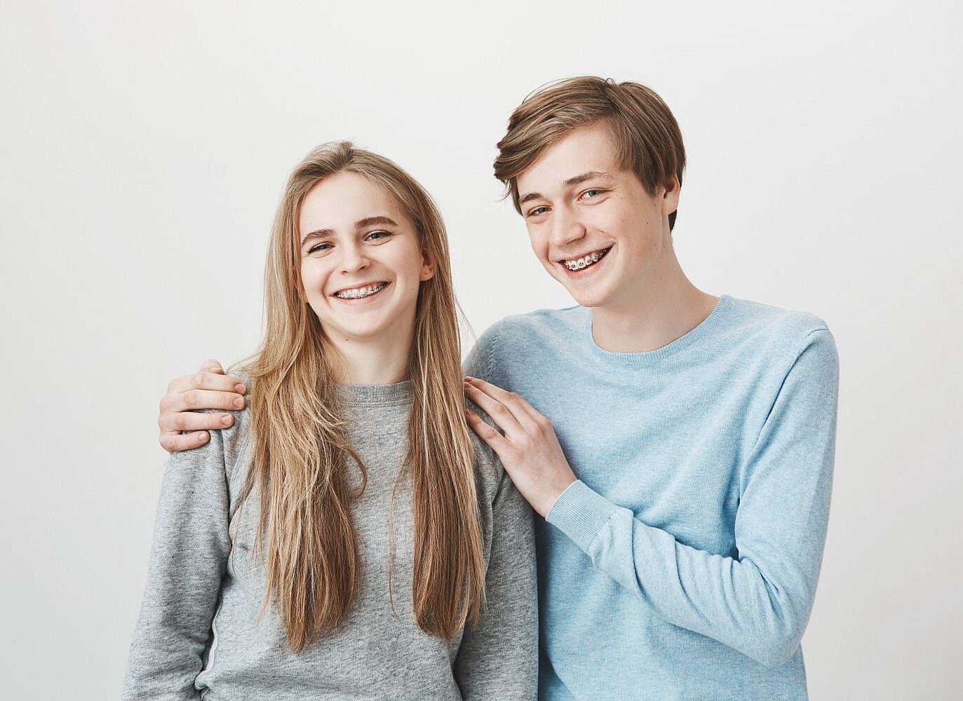 Smiling teens with metal braces at Tollison Orthodontics in Greenville, SC, stand side by side in casual shirts against a white background.
